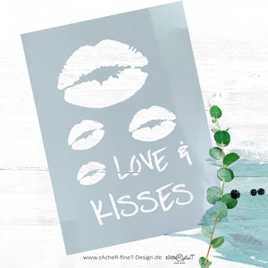 Könnte beinhalten: Ein hellblauer rechteckiger Druck mit weißen Lippenabdrücken und den Worten "LOVE & KISSES" in handschriftlicher Schrift. Der Druck ist abgewinkelt, mit einem Zweig grüner Blätter und türkisfarbenen und schwarzen Farbspritzern im Hintergrund.