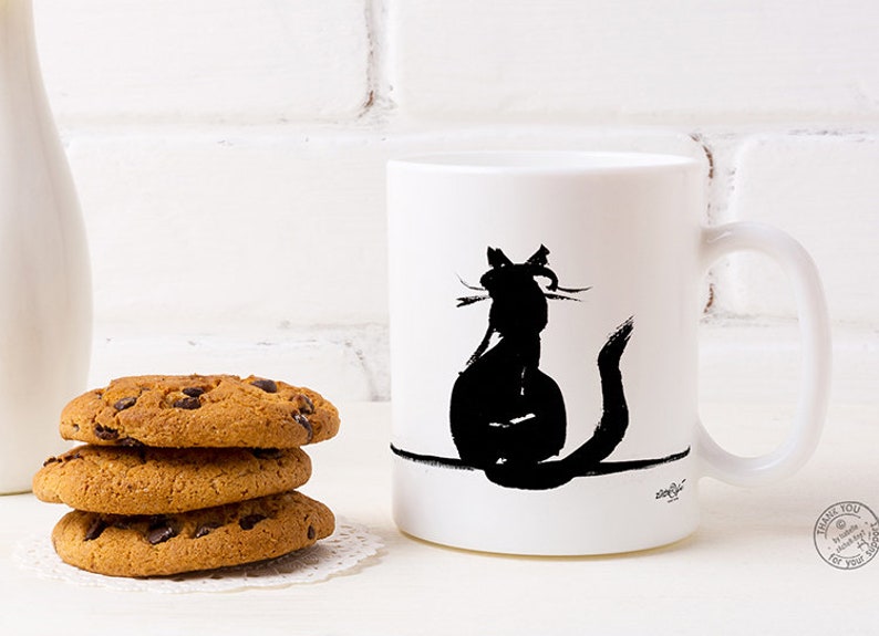 May include: White ceramic mug featuring a black cat silhouette. The cat is depicted from behind. Three chocolate chip cookies are stacked on a white doily beside the mug.