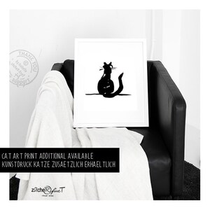 May include: A monochrome cat art print in a white frame. The image shows a black silhouette of a cat. The framed print is on a black leather chair with a white throw. Text at the bottom reads "CAT ART PRINT ADDITIONAL AVAILABLE".