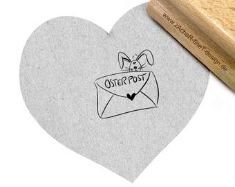 Può includere: Un timbro in gomma con un design a forma di cuore. Il timbro presenta un coniglio dei cartoni animati che sbircia da una busta con il testo "Oster Post" su di essa.