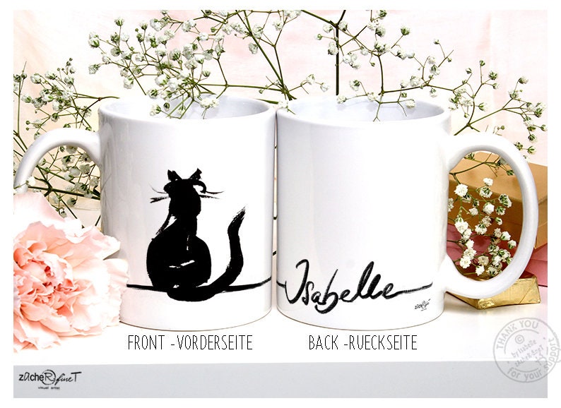 May include: Two white ceramic mugs. One mug features a black silhouette of a cat and the text "FRONT - VORDERSEITE". The other mug has the name "Isabelle" in black script and the text "BACK - RUECKSEITE".