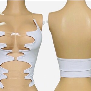 May include: White crop top with cut-out design and clear straps. The top features a unique, asymmetrical pattern with multiple openings and a band at the waist. The back of the top is a solid white band. A modern and stylish garment.