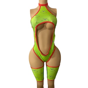 Puede incluir: Traje de baño de una pieza verde y rojo con estampado de Grinch. El traje de baño tiene un escote alto y un corte en la parte delantera. Las piernas están cubiertas con polainas a juego.