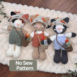 May include: Three crocheted cat dolls wearing hats and overalls, each carrying a small brown bag with colorful items. The dolls are calico, tan, and black and white. A gray rectangular box with the text No Sew Pattern is visible.