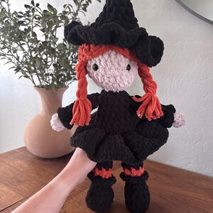 May include: A handmade crochet witch doll with a black hat and dress, and orange yarn braids. The doll has a pink face and black button eyes. The witch doll is approximately 10 inches tall.