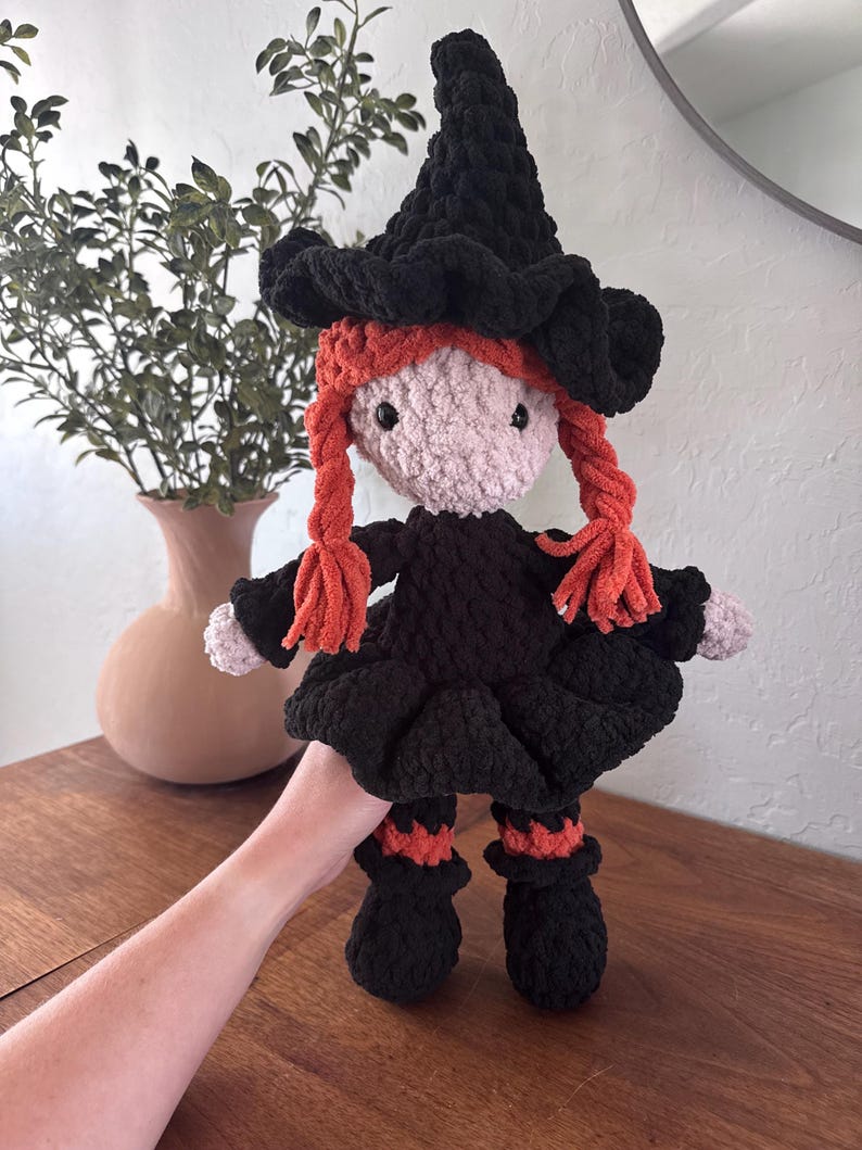 May include: A handmade crochet witch doll with a black hat and dress, and orange yarn braids. The doll has a pink face and black button eyes. The witch doll is approximately 10 inches tall.