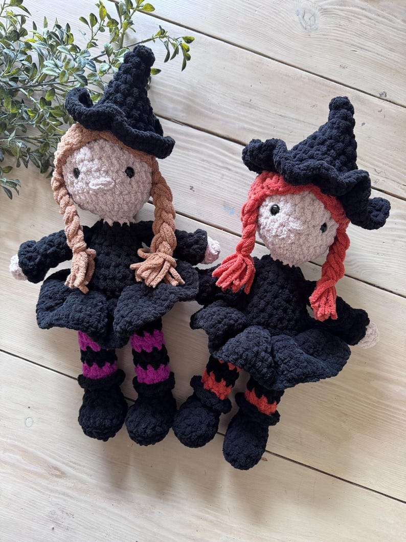 May include: Two handmade crochet witch dolls. Each doll has a black witch hat, black dress, and braided hair. One doll has tan braids, the other has red braids. The dolls have black shoes and striped socks in purple and orange.