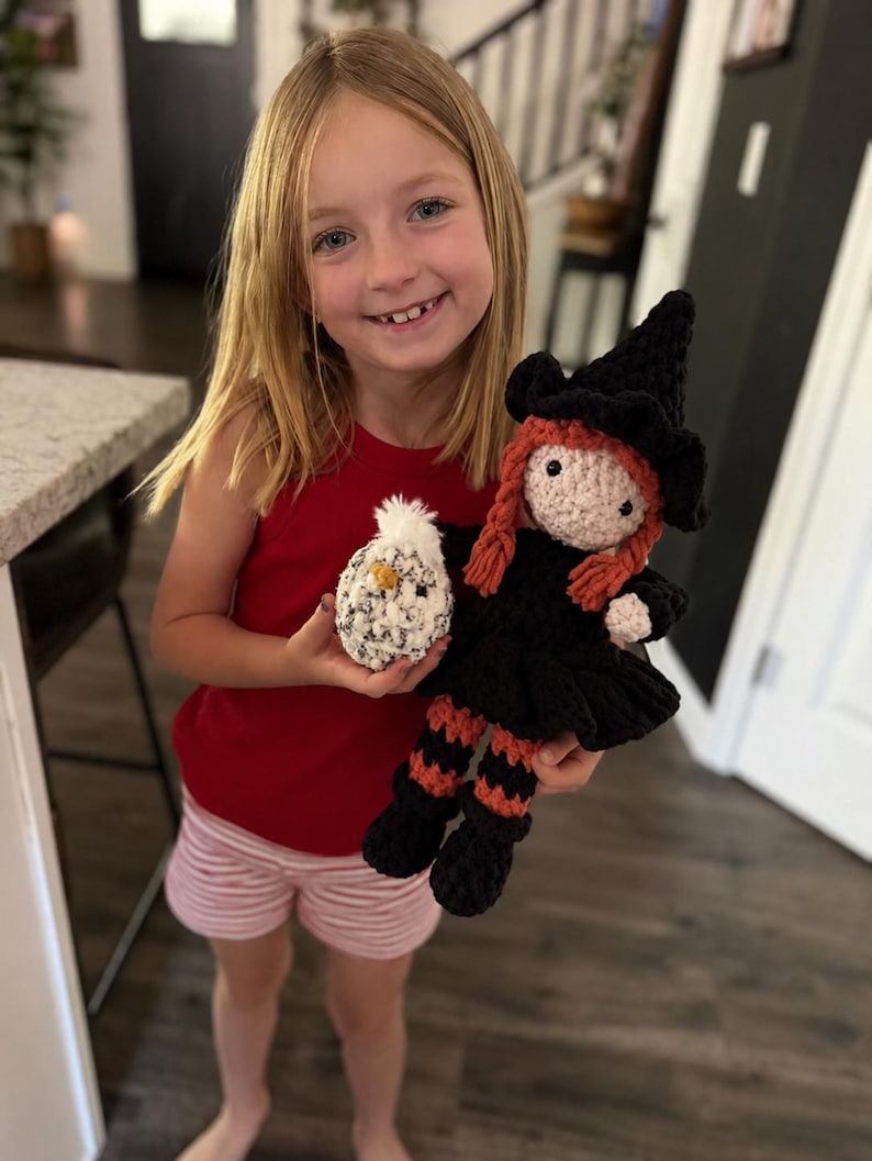 Young girl holding a handmade crochet witch doll and plush chick, showing the finished size of the Halloween crochet pattern.
