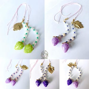 May include: A collection of handmade strawberry-themed jewelry. Each piece features a pair of strawberry charms in various colors, accented with white polka dots, strung with beads, and a gold-colored leaf charm.