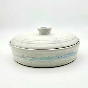 May include: A white ceramic serving dish with a lid. The dish has a light blue glaze with a subtle marbled effect. The lid has a small knob on top.