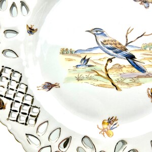 May include: White porcelain plate with a decorative openwork border and a hand-painted bird and butterfly design. The plate features a detailed illustration of a blue and brown bird perched on a branch, with several butterflies scattered around the rim.