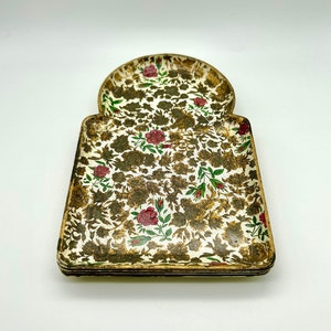 Könnte beinhalten: Ein dekoratives Tablett mit einem goldenen und weißen Blumenmuster mit roten Rosen. Das Tablett hat eine einzigartige gewölbte Form und ist aus einem leichten Material gefertigt.