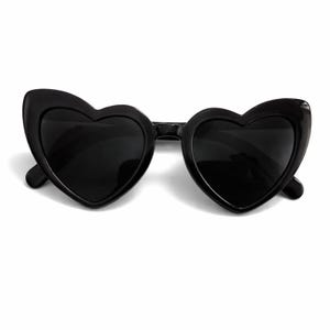 May include: A pair of black sunglasses featuring heart-shaped frames and dark, solid black lenses. The frames are constructed from a smooth, glossy black material, creating a distinct heart silhouette that encompasses both lenses.