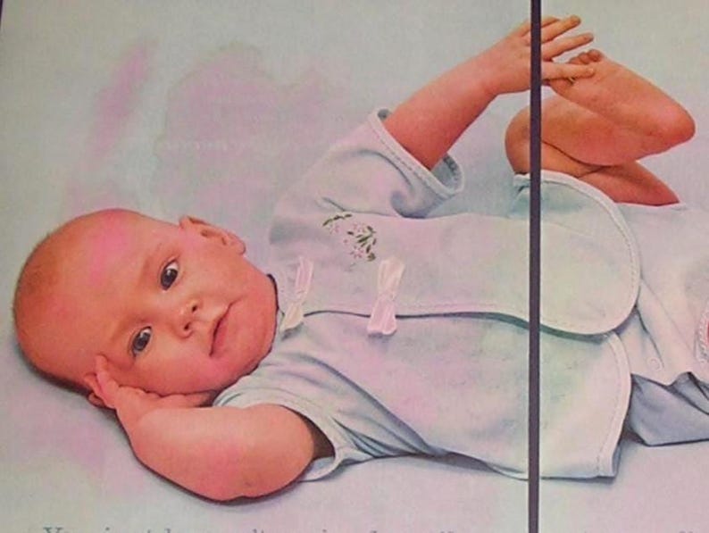 Puede incluir: Un beb&eacute; con un body azul claro con ribete blanco y un babero, acostado sobre una superficie azul claro. El beb&eacute; mira al espectador con una mano cerca de su cara y el otro brazo y pierna levantados.