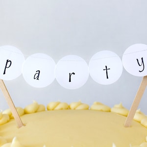 May include: A white cake with yellow frosting and a white paper party banner that says "party" in black lettering.