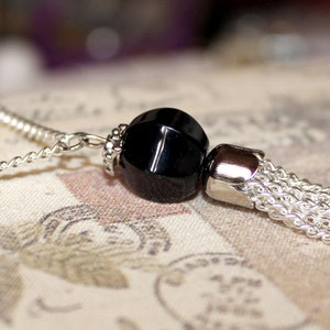May include: A black bead necklace with a silver chain and a silver tassel. The bead is faceted and has a high shine.