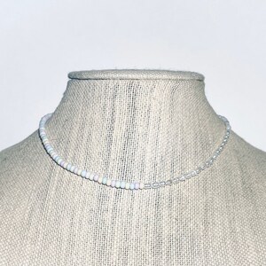 May include: A delicate white and pastel beaded necklace with a clear beaded section in the center.