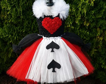 May include: A dress featuring a black crocheted bodice with a red heart appliqué, a white tulle collar, and a layered tulle skirt in red, black, and white. The white front panel of the skirt is decorated with two black spade playing card symbols.