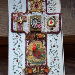May include: A decorative cross with religious imagery and embellishments. The cross has embroidered details, including a heart, stars, and floral accents. The base is white with a floral pattern.