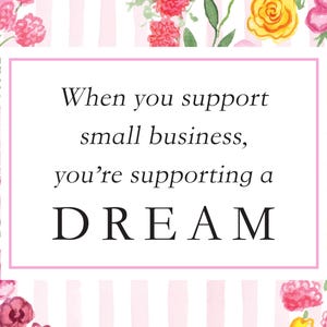 May include: A rectangular sign with a white background and light pink vertical stripes, framed by watercolor flowers in shades of pink, yellow, and green. The text reads: When you support small business, you&rsquo;re supporting a DREAM.