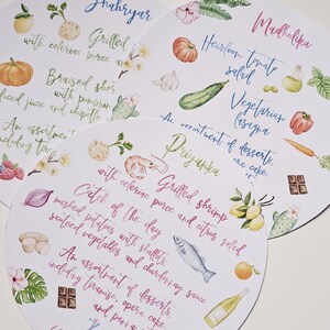 May include: Three white round paper place cards with watercolour illustrations and handwritten text. The place cards list the menu items for a wedding reception. The first place card says "Shahryar" and lists "Grilled Shrimp with celeriac puree and citrus salad". The second place card says "Madhulika" and lists "Heirloom Tomato Salad, Vegetarian Lasagna, An assortment of desserts, one cake". The third place card says "Priyanka" and lists "Catch of the Day, Mashed potatoes with shallots, sauteed vegetables and Chardonnay sauce, An assortment of desserts, including tiramisu, opera cake, and panna cotta".