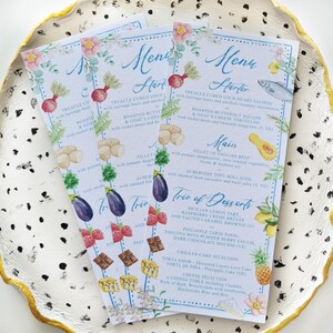May include: A set of three watercolour menus with floral borders and illustrations of food. The menus list a starter, main course, and a trio of desserts. The text on the menus reads: "Menu Starter", "Treacle Cured Loch Duart Salmon", "Roasted Butternut Squash", "Main", "Fillet of English Beef", "Trio of Desserts", "Sicilian Lemon Tart", "Raspberry Creme Brulee", "Pineapple Tarte Satin", "Chillian Themes Selection".