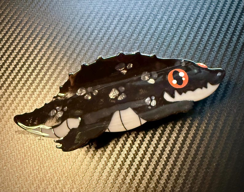 May include: A black and white alligator-shaped decorative object with red eyes and white teeth. The alligator has a textured, glossy finish with silver accents. The object is likely a decorative figurine or trinket.