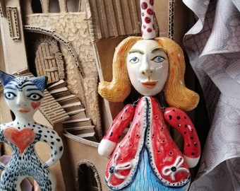 Ceramic little doll on a string. Hanging ceramic sculpture or pottery clay. Girl in a red dress, with moving head, arms and legs.