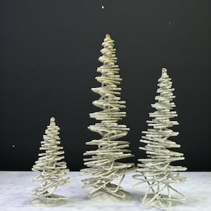 May include: Three decorative Christmas trees in varying sizes. Each tree is made of twisted, off-white rope, creating a textured, spiral design. The trees stand on white circular bases, perfect for holiday decor.