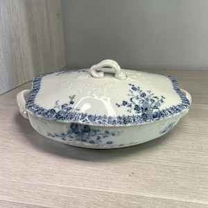 May include: A white porcelain serving dish with a lid. The dish features a blue floral pattern around the edges and on the lid. The lid has a handle and the dish has two side handles.