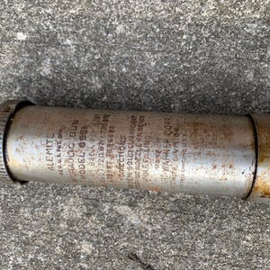 May include: A vintage Alemite Model 655 hydraulic gun, cylindrical in shape, with visible text including "Alemite" and "Hydraulic Gun." The metal body shows signs of age and wear, with a threaded end and a nozzle. The text provides instructions for use.
