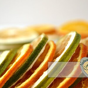 May include: Dried orange and lime slices stacked on top of each other. The slices are a vibrant orange and green color. The background is white. The image has a logo for "Natural Crafts" in the bottom right corner.