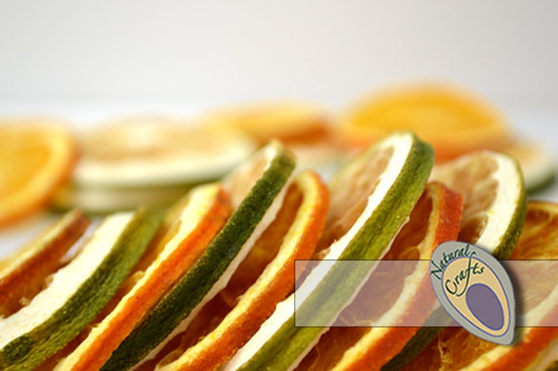 May include: Dried orange and lime slices stacked on top of each other. The slices are a vibrant orange and green color. The background is white. The image has a logo for "Natural Crafts" in the bottom right corner.