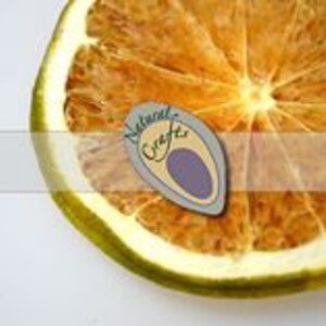 May include: A close-up of a dried orange slice, showing the texture and color of the fruit. The slice is light brown with a yellow outer edge. The center of the slice is a lighter shade of brown. The slice is on a white background.