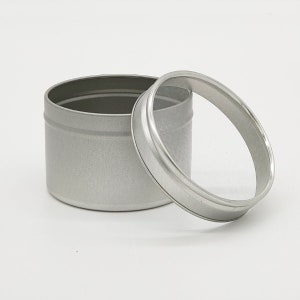 May include: A silver metal container with a clear lid. The container is cylindrical and has a smooth, shiny finish.