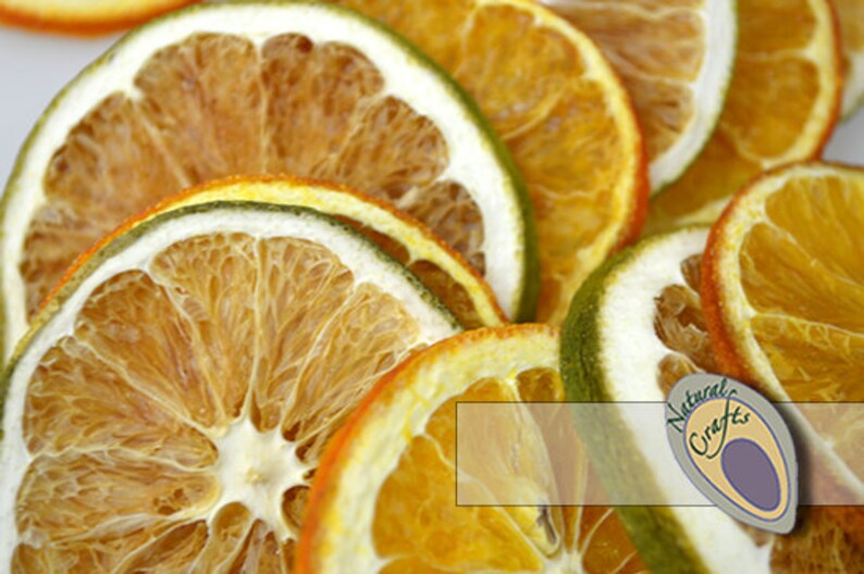 May include: Dried orange and lime slices, arranged in a pile. The slices are a mix of yellow, orange, and green colors. The image has a white background and the text "Natural Crafts" in the bottom right corner.