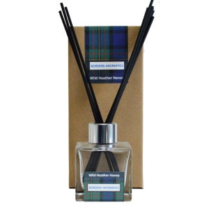 May include: A clear glass bottle with a silver lid and black diffuser sticks. The bottle is labelled "Wild Heather Honey" and "Borders Aromatics". The label has a plaid pattern in blue, green and red.