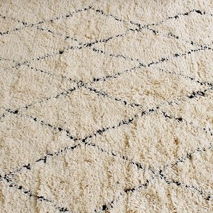 May include: A white shag rug with a black diamond pattern. The rug is made of soft, fluffy fibers and has a subtle sheen.