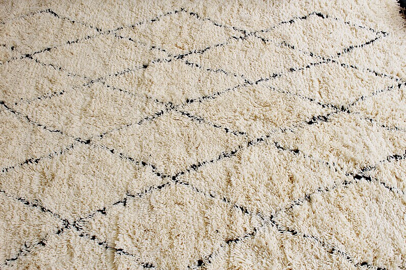 May include: A white shag rug with a black diamond pattern. The rug is made of soft, fluffy fibers and has a subtle sheen.