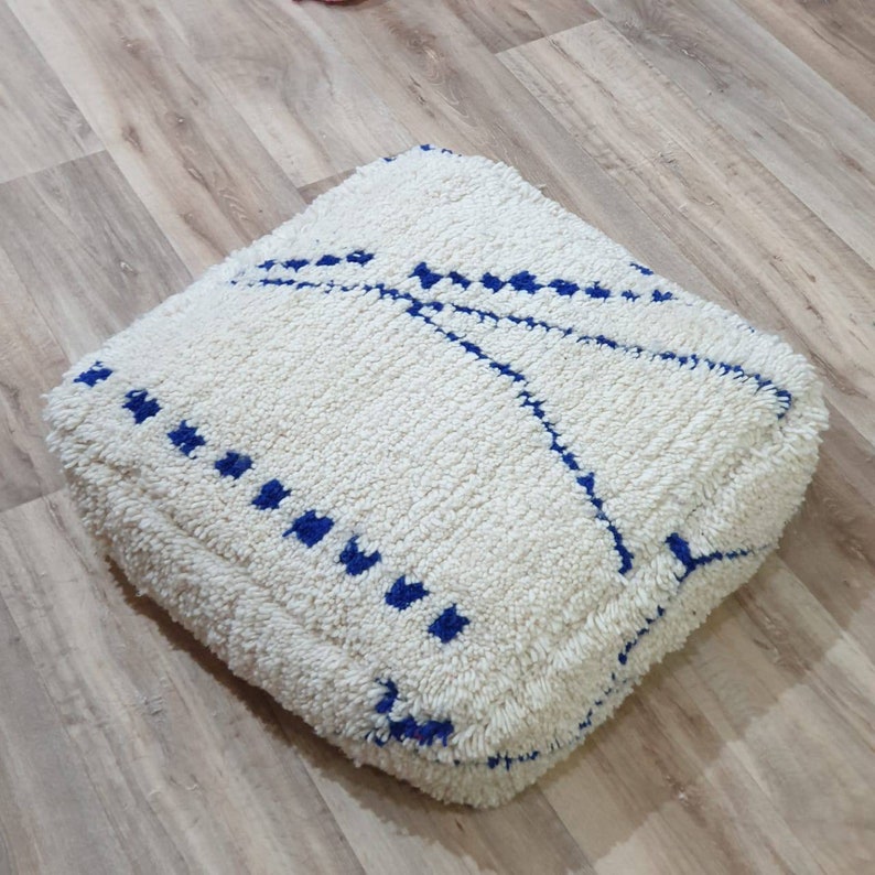 K&ouml;nnte beinhalten: Ein wei&szlig;er Bodenkissen mit einem blauen geometrischen Muster. Das Kissen ist aus einem weichen, flauschigen Material und hat eine quadratische Form.