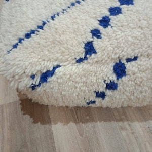K&ouml;nnte beinhalten: Wei&szlig;er und blauer marokkanischer Pouf mit einer flauschigen Textur. Der Pouf hat ein geometrisches Muster aus blauen Quadraten und Rauten.