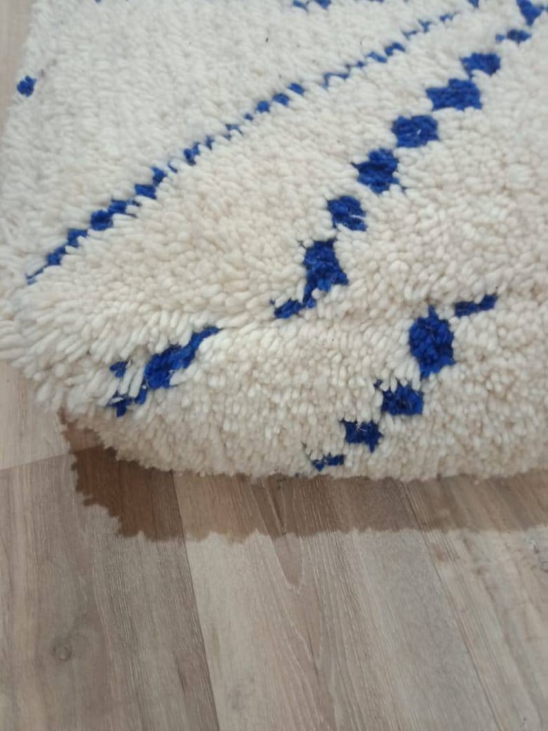 K&ouml;nnte beinhalten: Wei&szlig;er und blauer marokkanischer Pouf mit einer flauschigen Textur. Der Pouf hat ein geometrisches Muster aus blauen Quadraten und Rauten.