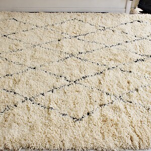 May include: A white shag rug with a black diamond pattern. The rug has a soft, fluffy texture.