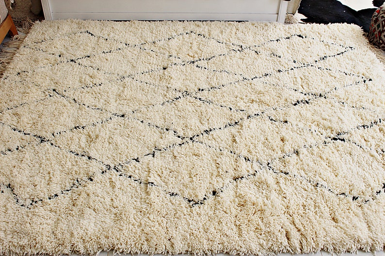 May include: A white shag rug with a black diamond pattern. The rug has a soft, fluffy texture.