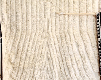 May include: A white, fluffy rug with a geometric pattern. The rug has a fringe border and is hanging on a wall.