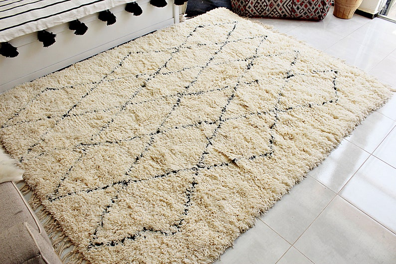 May include: A cream-colored rug with a black diamond pattern. The rug has a shaggy texture and is made of wool.