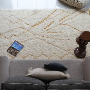 May include: A white and gold patterned rug with a gray couch and pillows, a wooden side table, and a magazine on the rug.