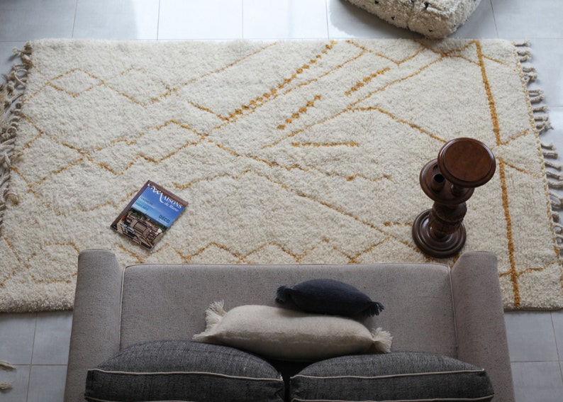 May include: A white and gold patterned rug with a gray couch and pillows, a wooden side table, and a magazine on the rug.