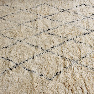 May include: A cream-colored rug with a diamond pattern woven in black thread. The rug has a fluffy, textured surface.
