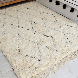 May include: A white shag rug with a black diamond pattern. The rug has fringe on all sides.